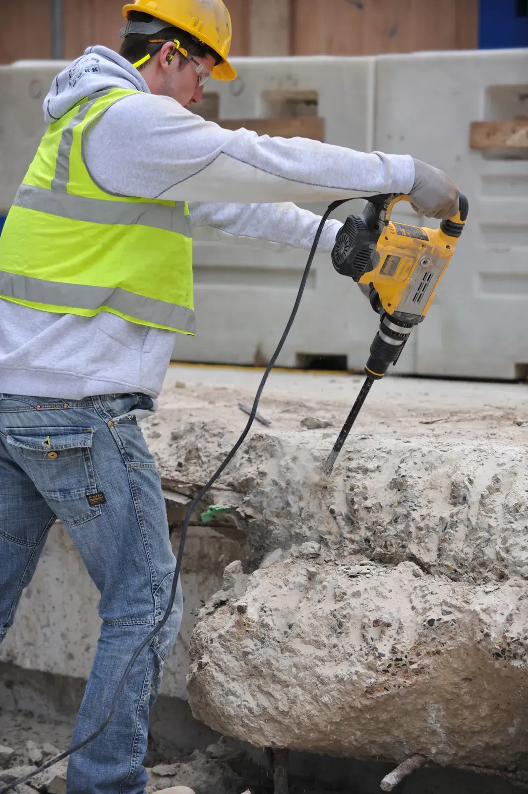 Arbeiter nutzt gelben DEWALT Bohrhammer zum Aufbrechen von Beton auf einer Baustelle.
