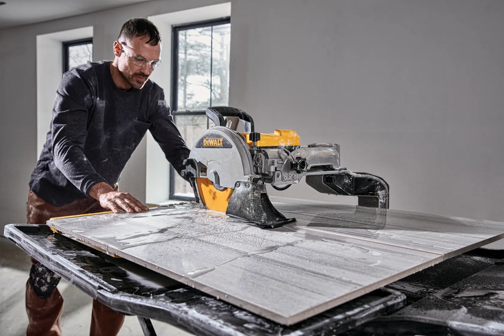 Eine Person verwendet eine DEWALT D36000 Fliesensäge, um eine große Fliese auf einem Arbeitstisch in einem Raum mit zwei Fenstern zu schneiden.