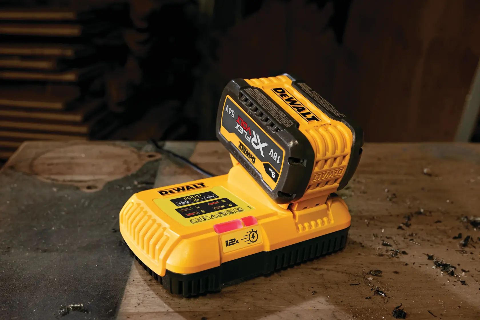 Ein gelbes DEWALT DCB117 Akku-Ladegerät mit angeschlossenem DEWALT XR FLEXVOLT 18V/54V Akku auf einer staubigen Werkbank.