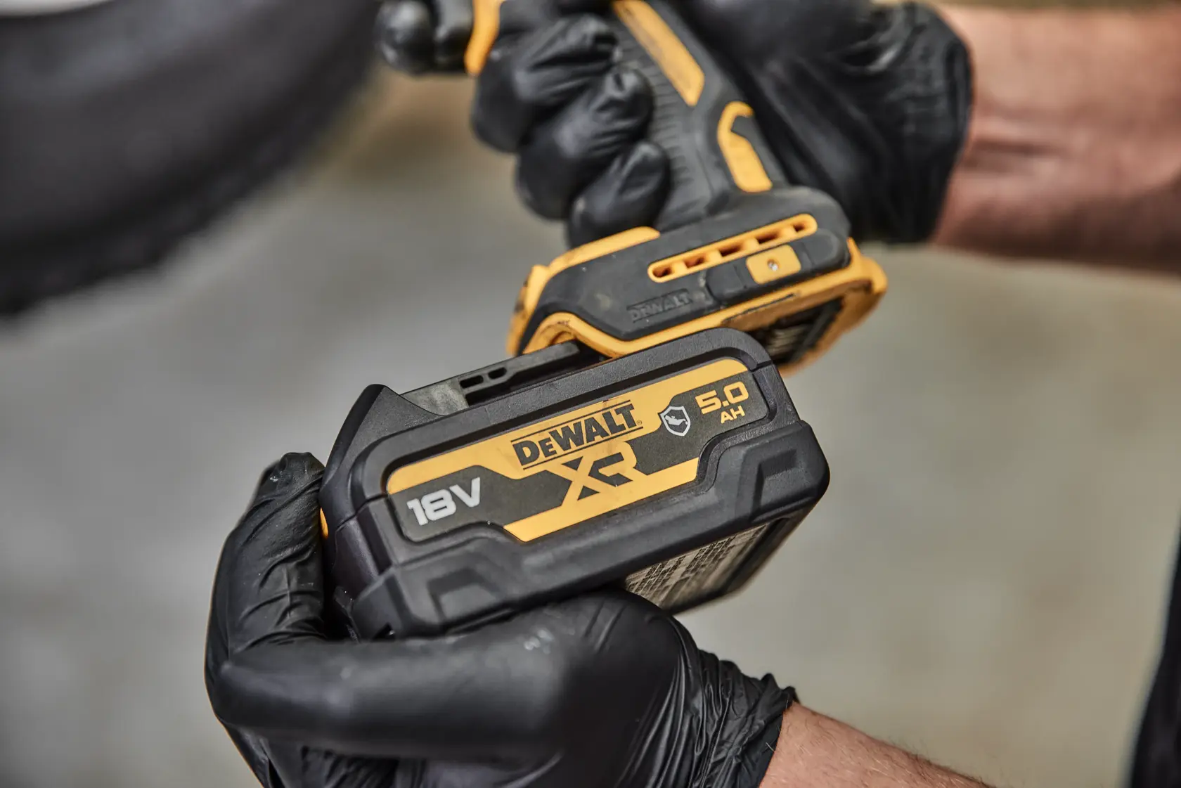 Nahaufnahme einer Person mit schwarzen Handschuhen, die ein kabelloses DEWALT Elektrowerkzeug mit angebautem DCB184G 18V XR Lithium-Ionen Akku hält.