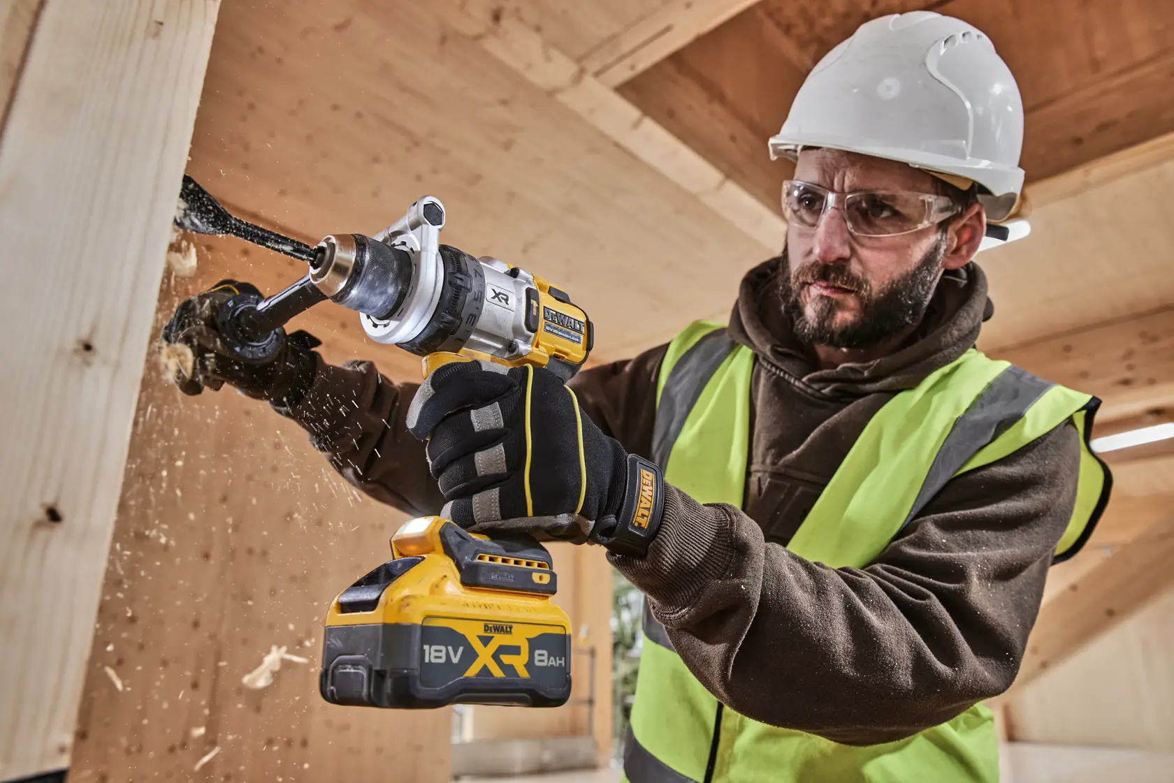 Person bohrt Holz mit DEWALT XR 18V 8Ah Akku-Bohrmaschine und trägt Sicherheitsausrüstung.