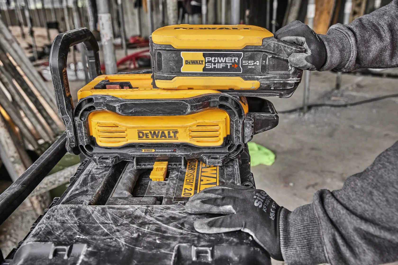 Batería DEWALT Power Shift colocada en dispositivo amarillo DEWALT en obra por mano con guante.