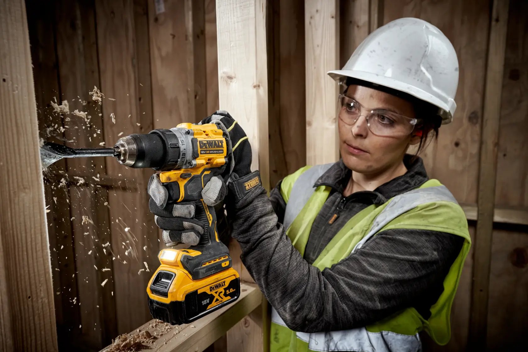 Person drills wood with DEWALT DCD800P2T in construction setting wearing helmet and gloves.