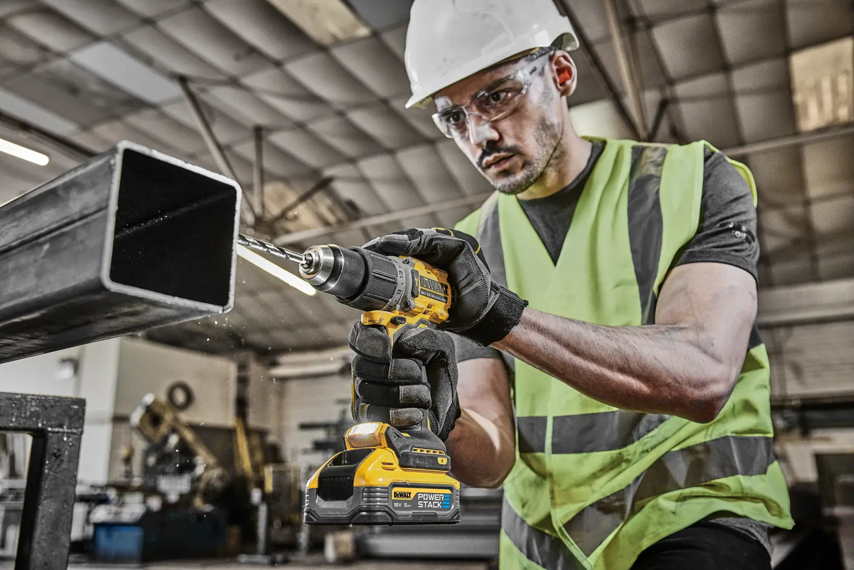 Trabajador usando taladro DEWALT en viga metálica, lleva equipo de seguridad y guantes.