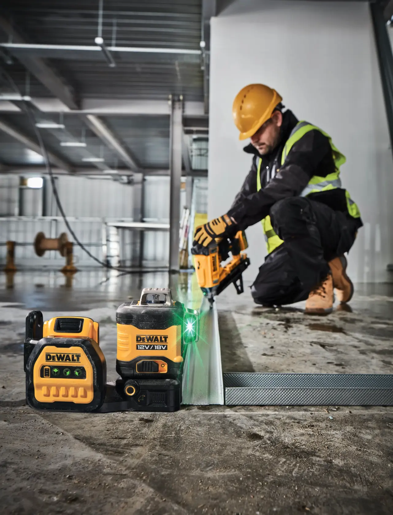 DEWALT Laser und Akku auf dem Boden; Arbeiter nutzt Werkzeug auf Baustelle.