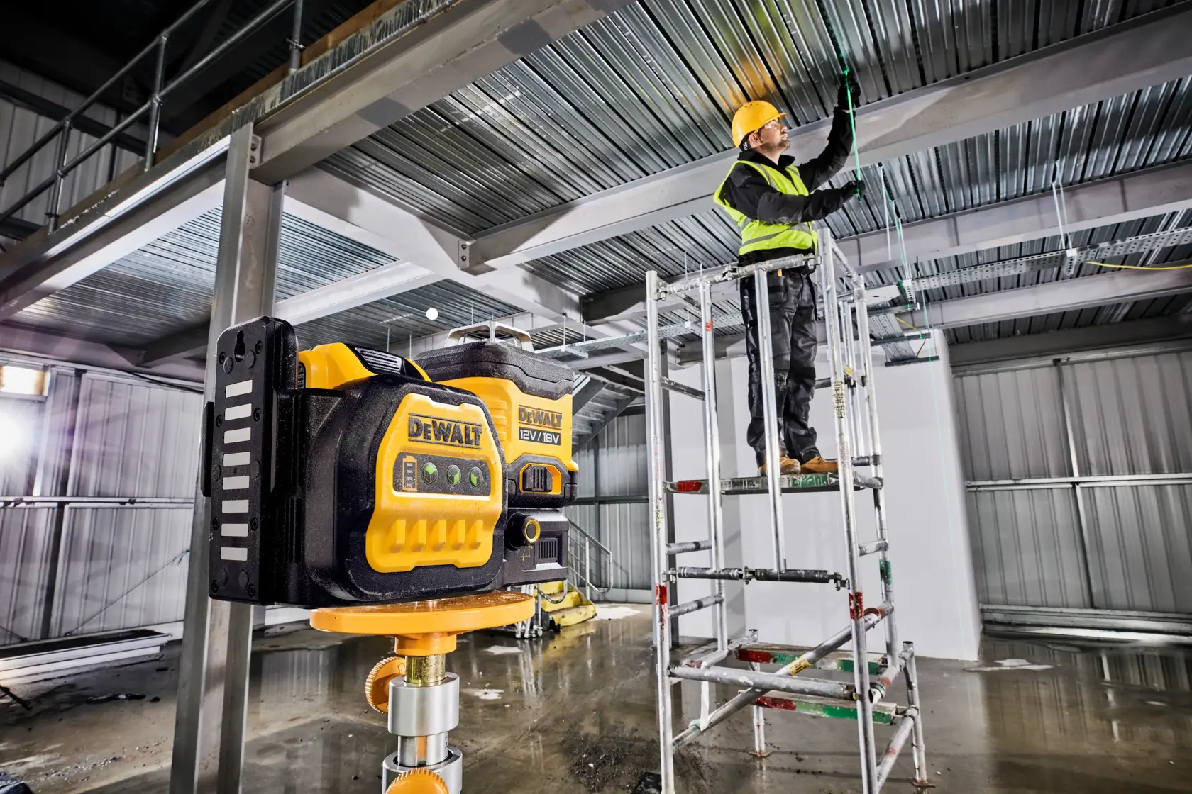 DEWALT-Laser auf Baustelle, Arbeiter justiert Deckenverkabelung auf einem Gerüst.
