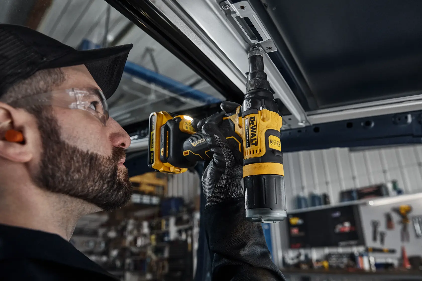 Una persona utiliza un destornillador inalámbrico DEWALT DCF403NT para atornillar en un marco metálico en un taller. El énfasis está en la herramienta y la mano enguantada del usuario.