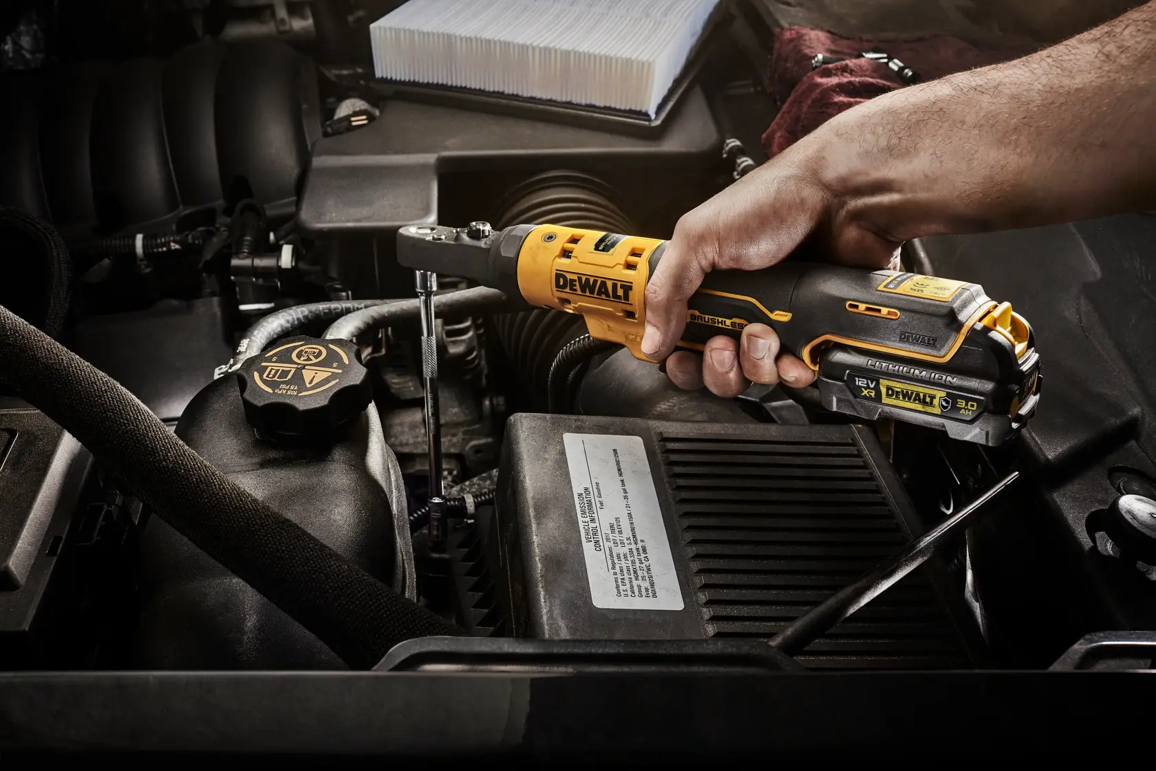 Mano usando trinquete inalámbrico DEWALT DCF500N en un motor de automóvil.