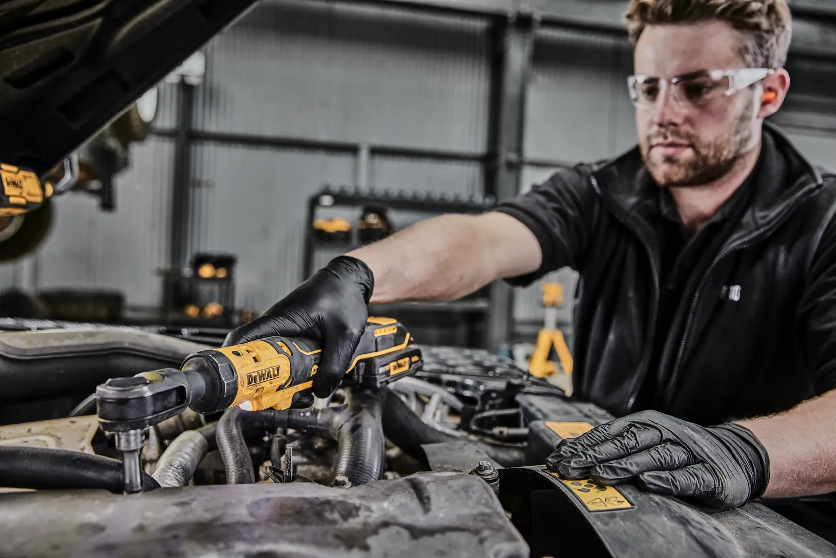 Eine Person mit schwarzen Handschuhen benutzt ein DEWALT DCF512N Akku-Ratschenwerkzeug, um am Motor eines Fahrzeugs zu