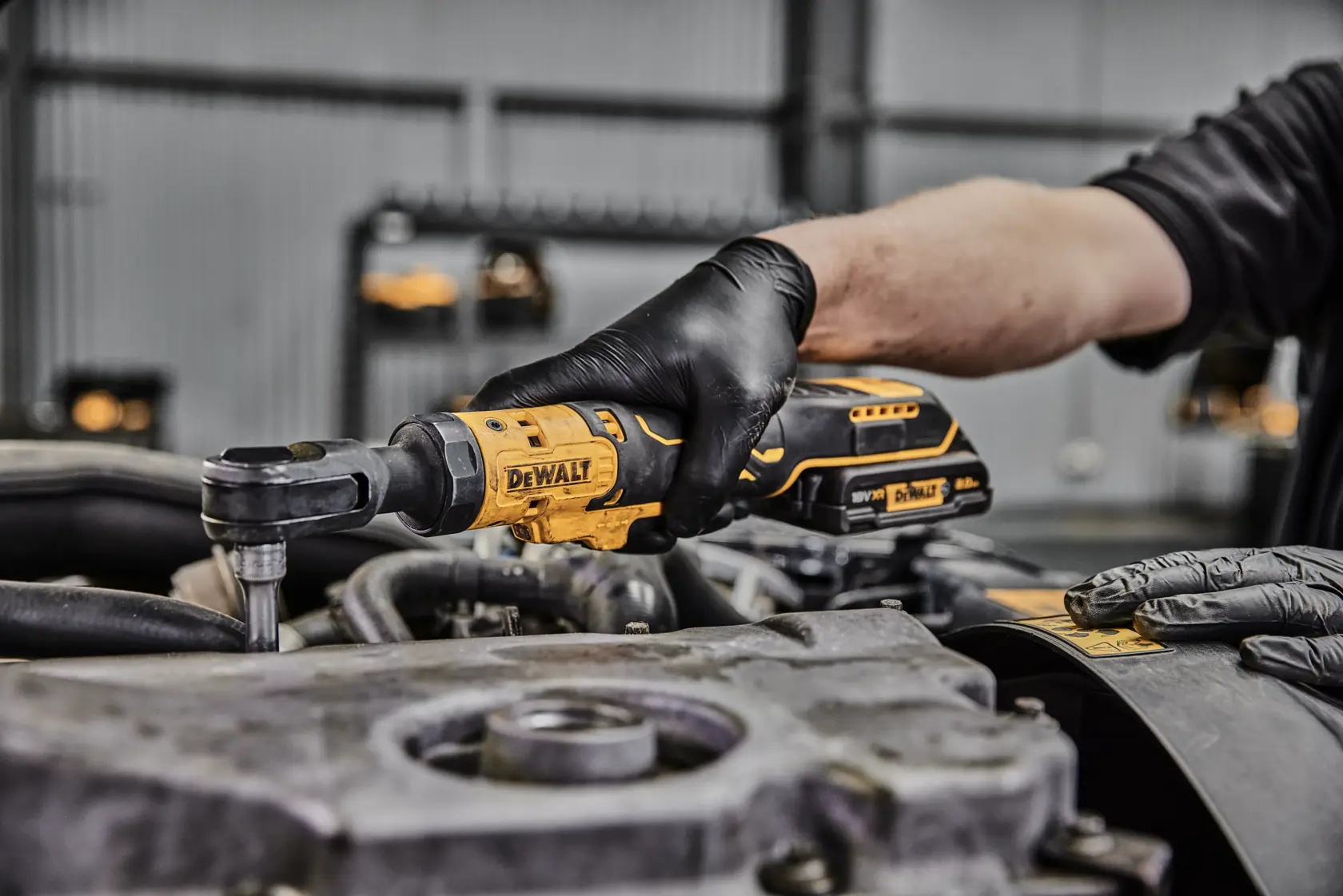 Eine Person mit schwarzen Handschuhen verwendet einen kabellosen DEWALT Ratschen-Schraubenschlüssel, um an einem Motorteil