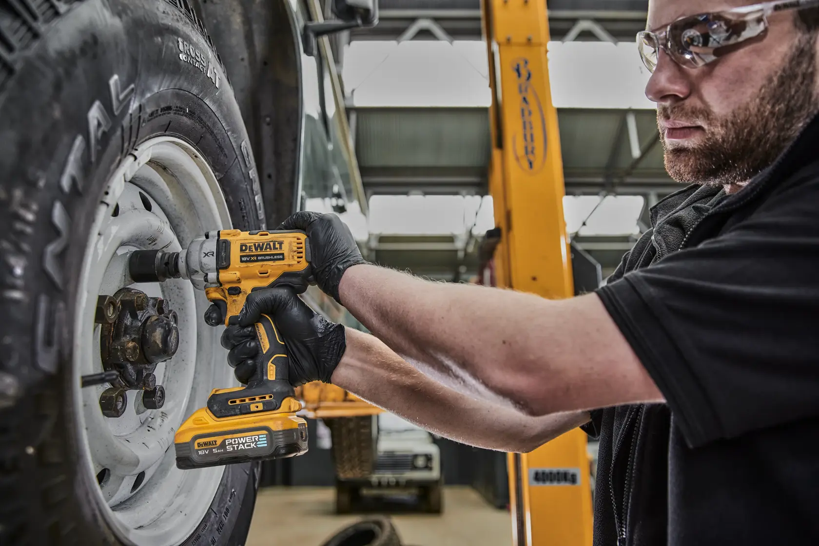 Una persona con guantes negros utiliza una llave de impacto inalámbrica DEWALT DCF891H2T para aflojar o apretar las tuercas de rueda de un vehículo en un taller.