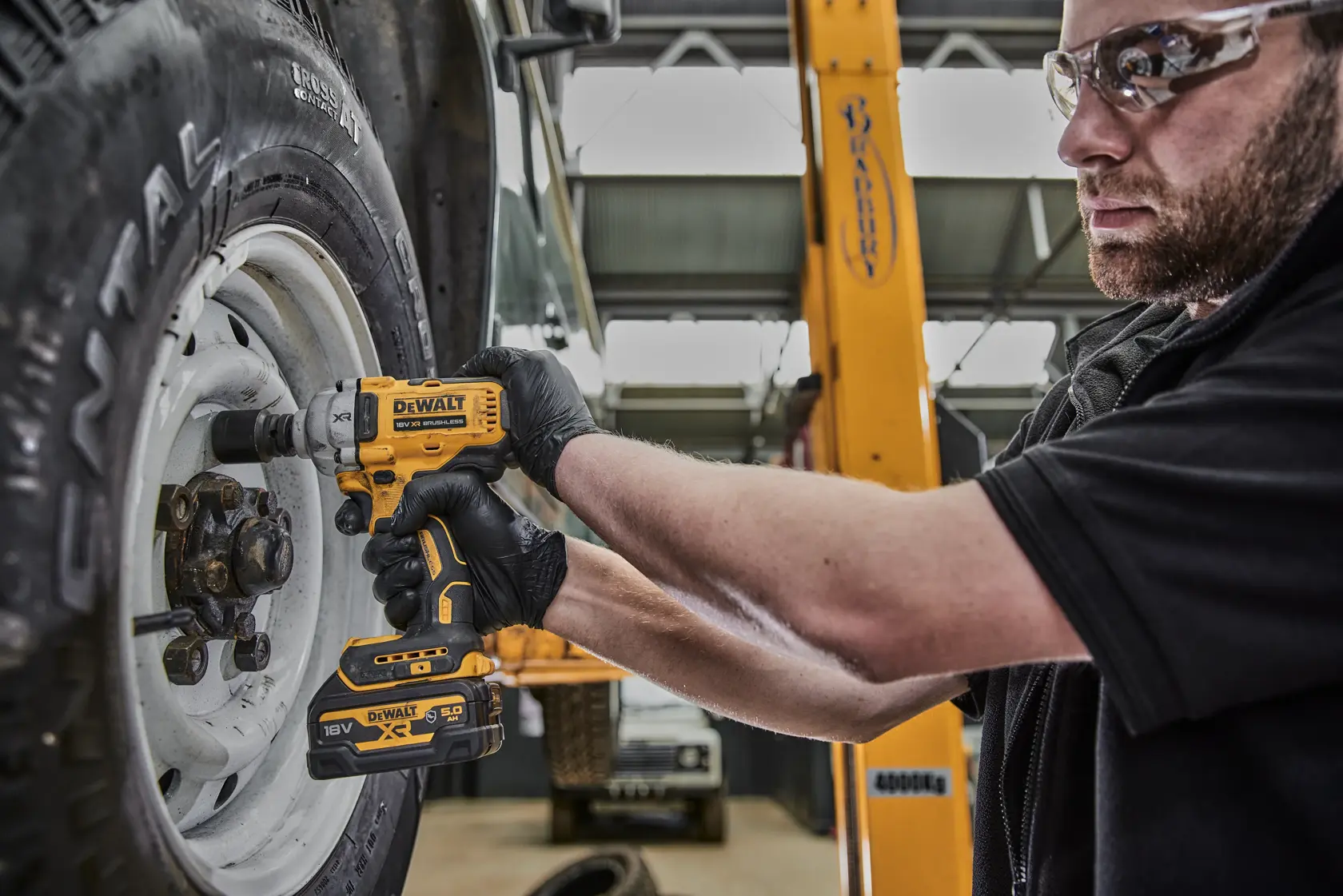 Person using a DEWALT DCF891N impact wrench to tighten a wheel on a vehicle in a workshop.