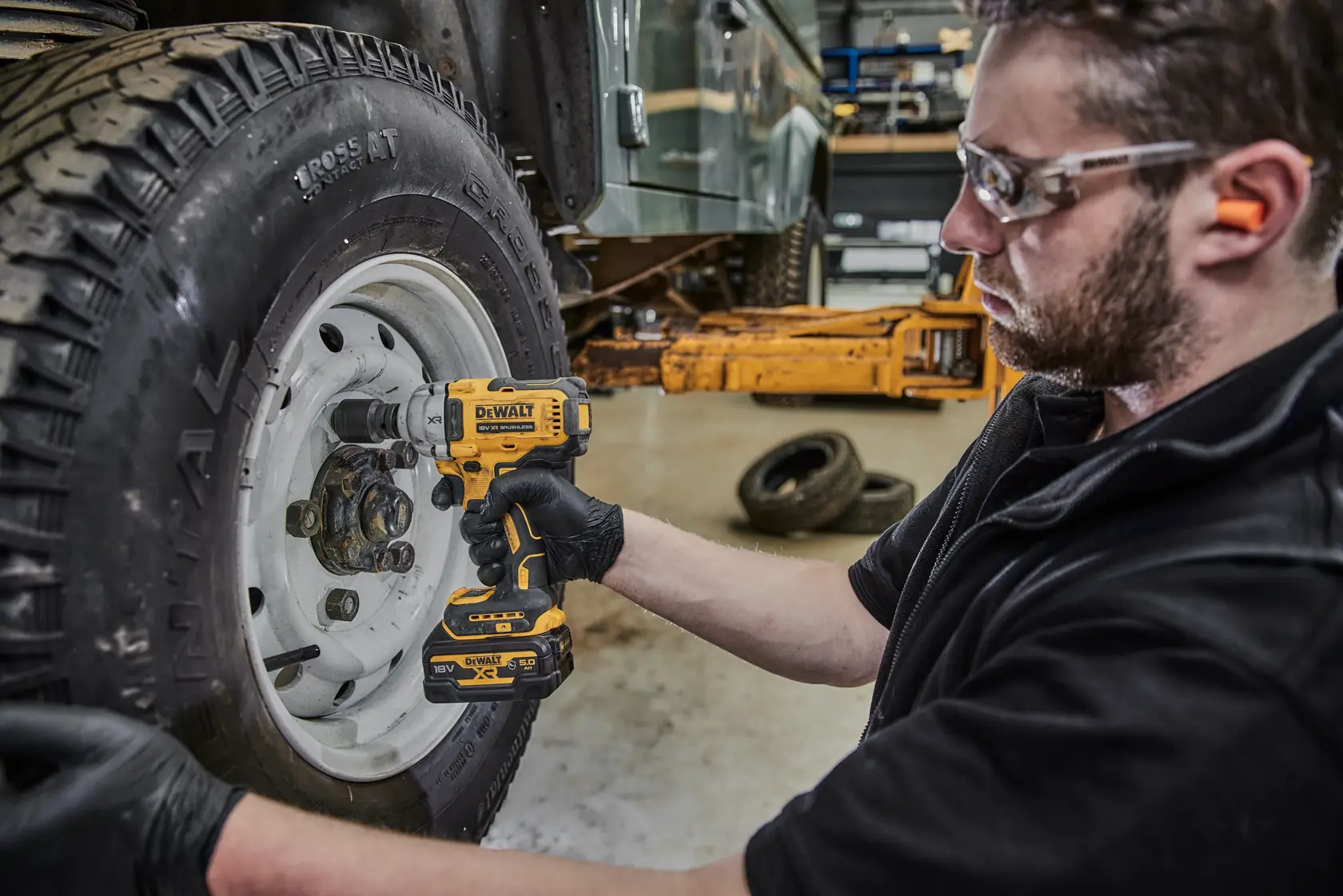 Person uses DEWALT DCF891N impact wrench to remove wheel lug nuts from vehicle in workshop.