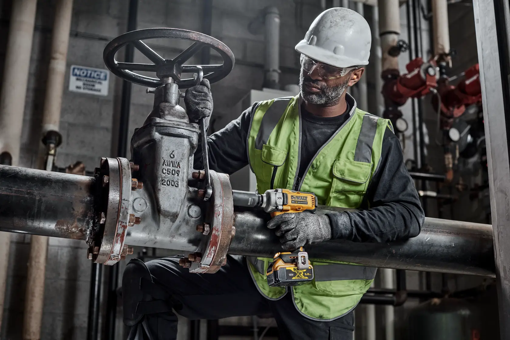 Worker uses DEWALT tools DCF892N, DCZ407P1T1-XE on industrial pipe in factory setting. Safety gear worn.