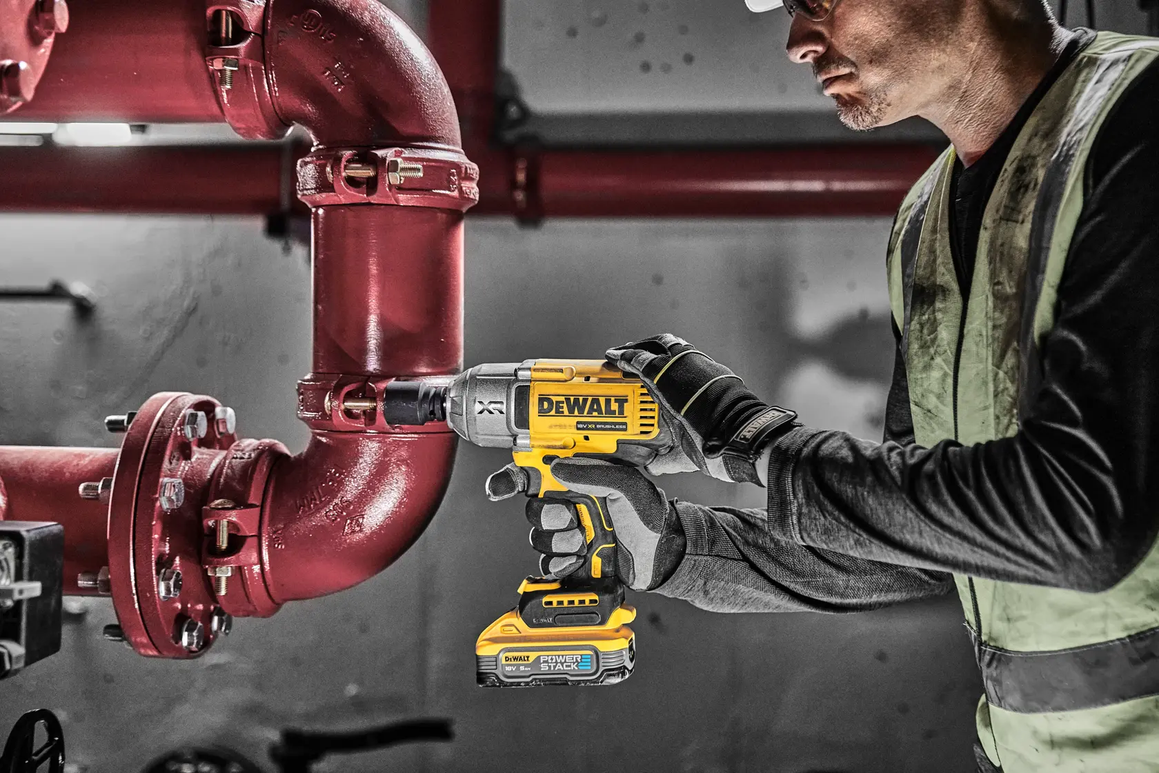 Persona usa llave de impacto DEWALT DCF900H2T en una tubería roja en entorno industrial.