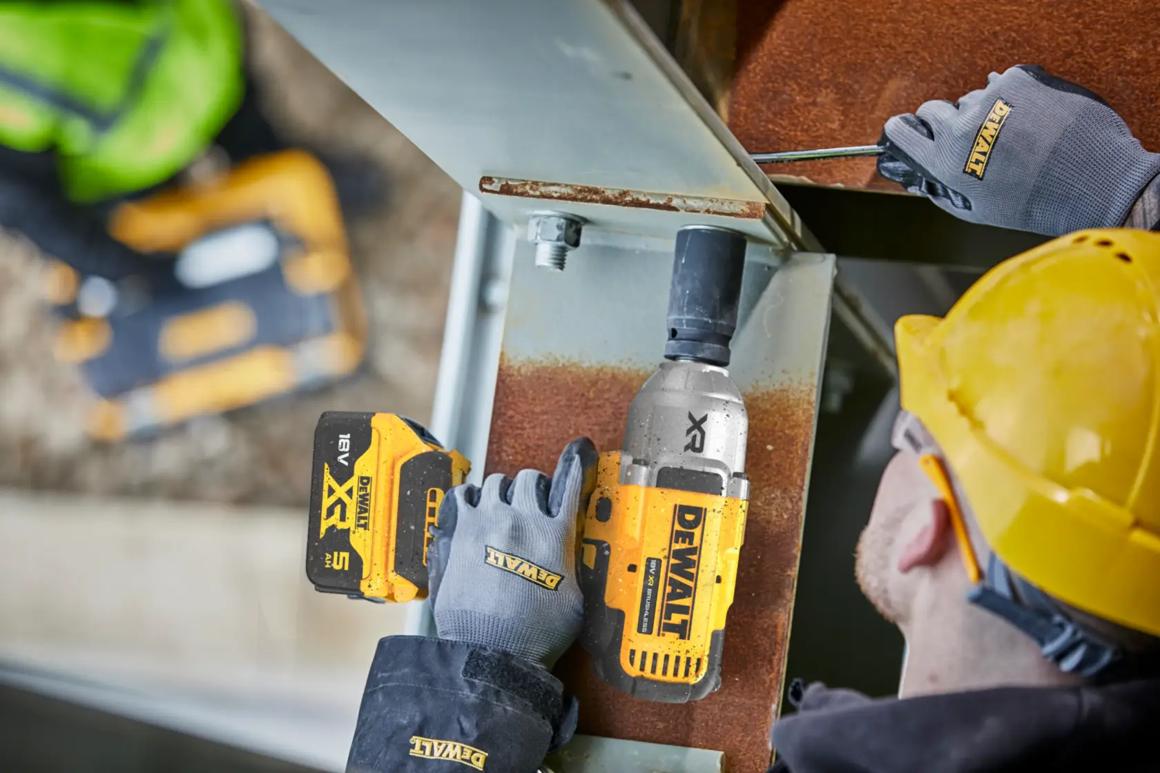 Worker using a DEWALT DCF900N impact wrench on a metal beam at a construction site, wearing gloves and helmet.
