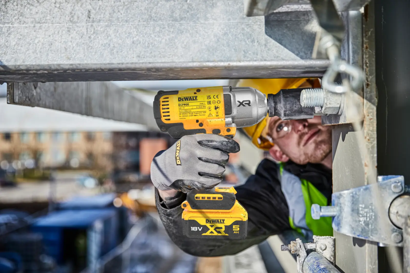 Trabajador utiliza llave de impacto DEWALT DCF900P2T en estructura metálica exterior. Batería y guantes visibles.