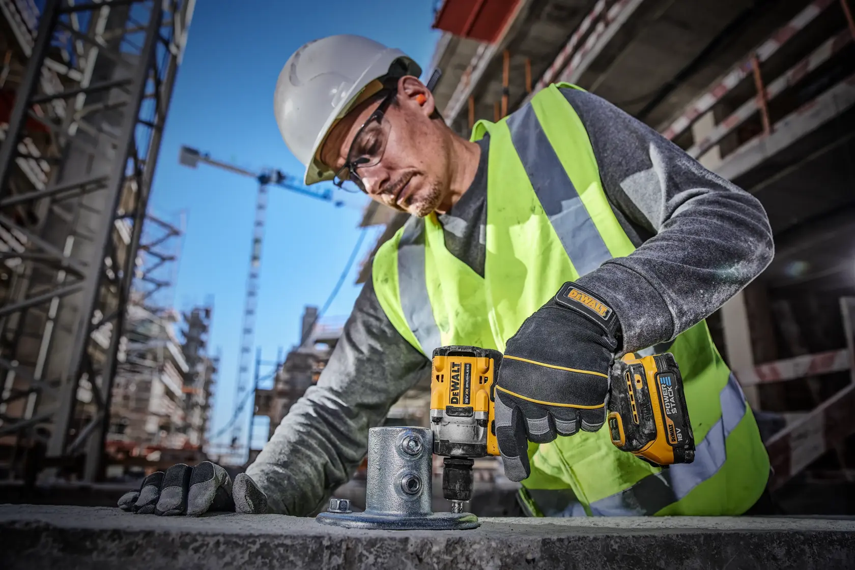 Imagen de una batería compacta DEWALT 18V XR Powerstack. La batería es de color amarillo y negro, con el logo de DEWALT y la etiqueta '18V POWERSTACK'. Debajo de la batería, el texto indica que DEWALT es la primera marca de herramientas eléctricas del mundo en utilizar baterías con celdas apiladas en bolsas, diseñadas para la industria de la construcción.