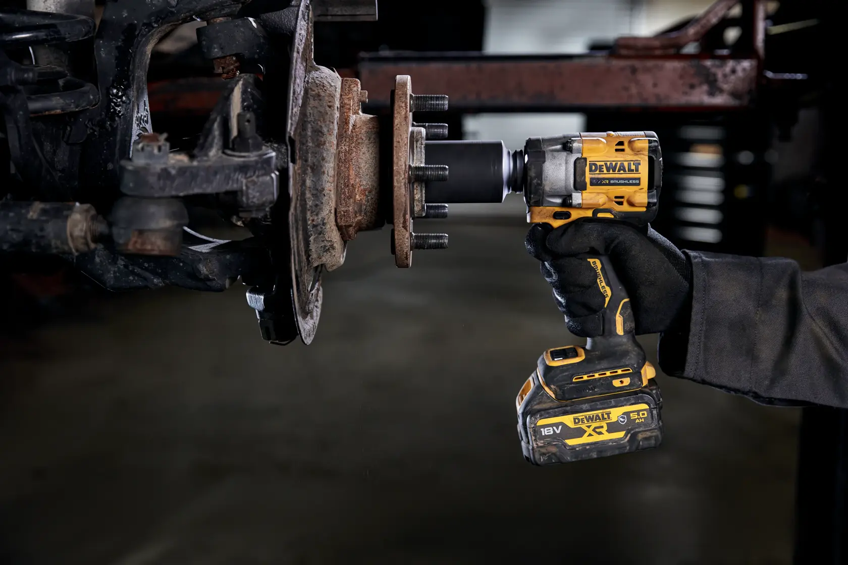 Eine Person verwendet einen DEWALT Akku-Schlagschrauber (Modell DCF923P2G), um an einer verrosteten Radnabe eines Fahrzeugs in einer Werkstatt oder Garage zu arbeiten.