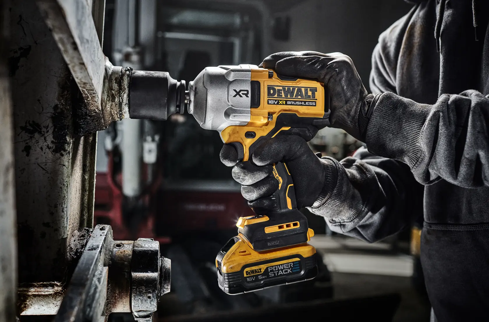 Llave de impacto inalámbrica DEWALT usada por manos enguantadas en metal, taller industrial.