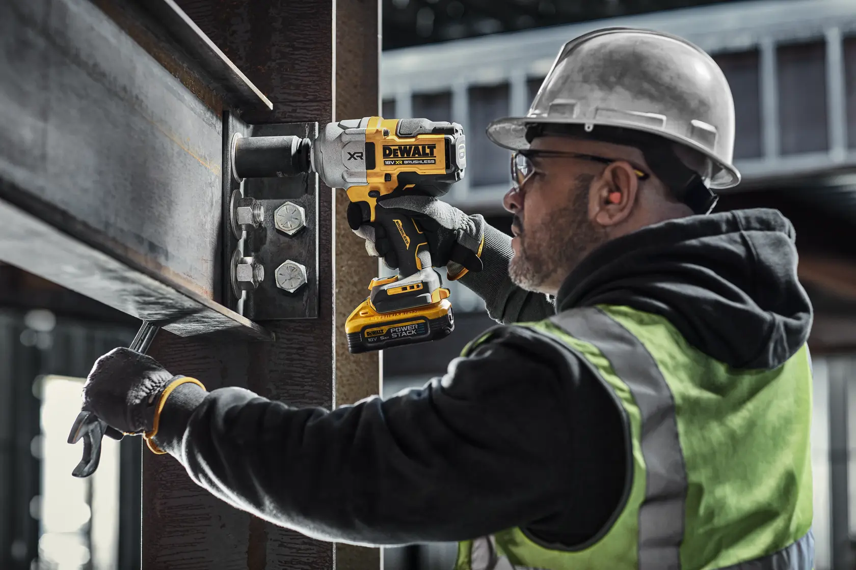 Persona usa llave de impacto DEWALT para ajustar tornillos en viga de acero de obra.
