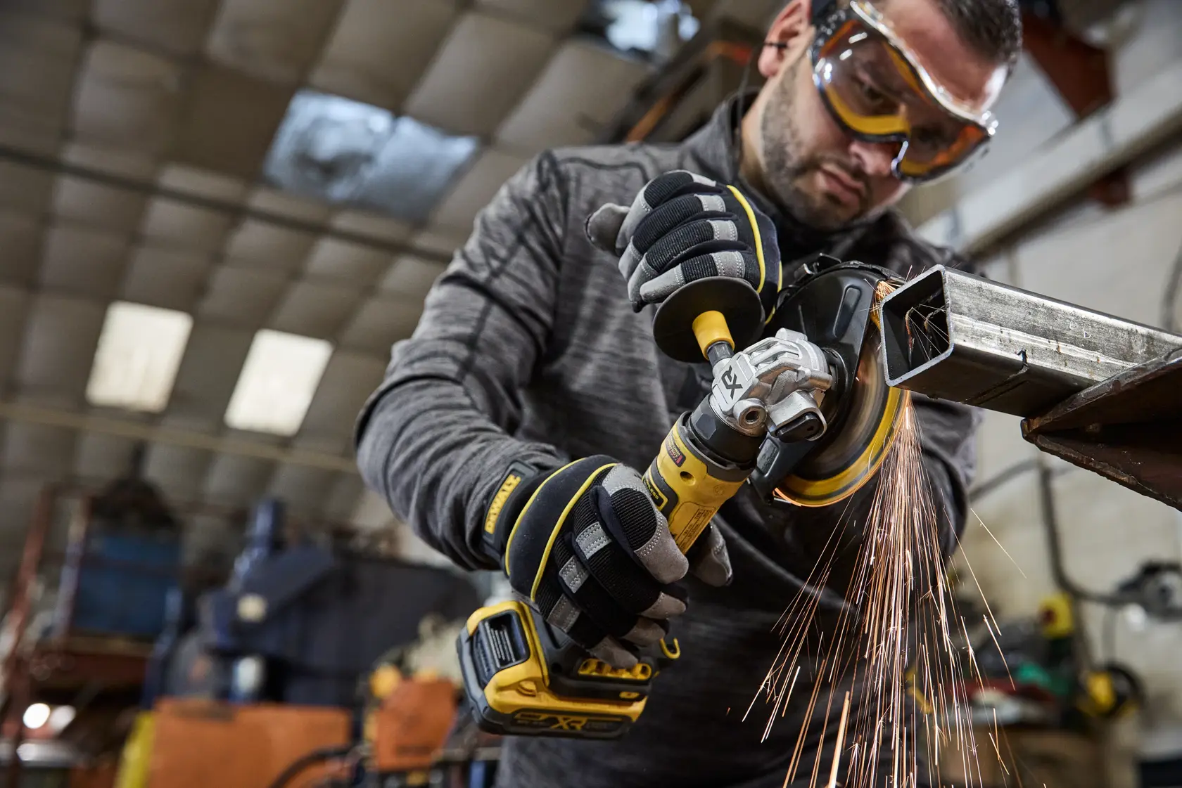 Persona usando una amoladora DEWALT inalámbrica en metal, con chispas, en un taller industrial.