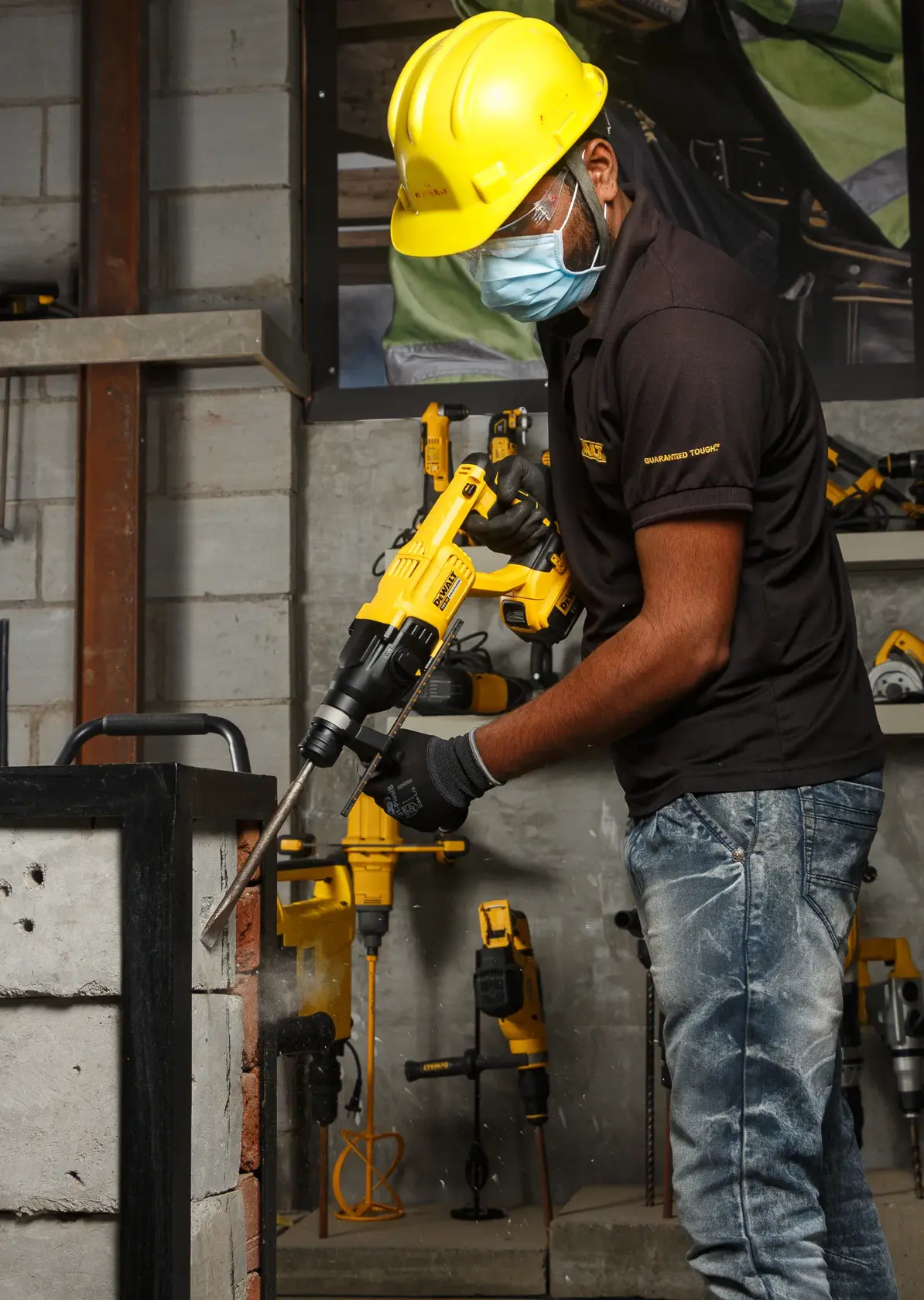 Trabajador usa DEWALT DCH133NT en un muro de cemento. Equipo protector y herramientas visibles.