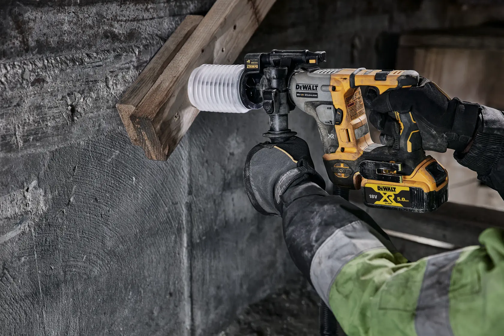 Martillo rotativo inalámbrico DEWALT perfora madera y concreto, usado por trabajador con guantes y chaqueta verde.