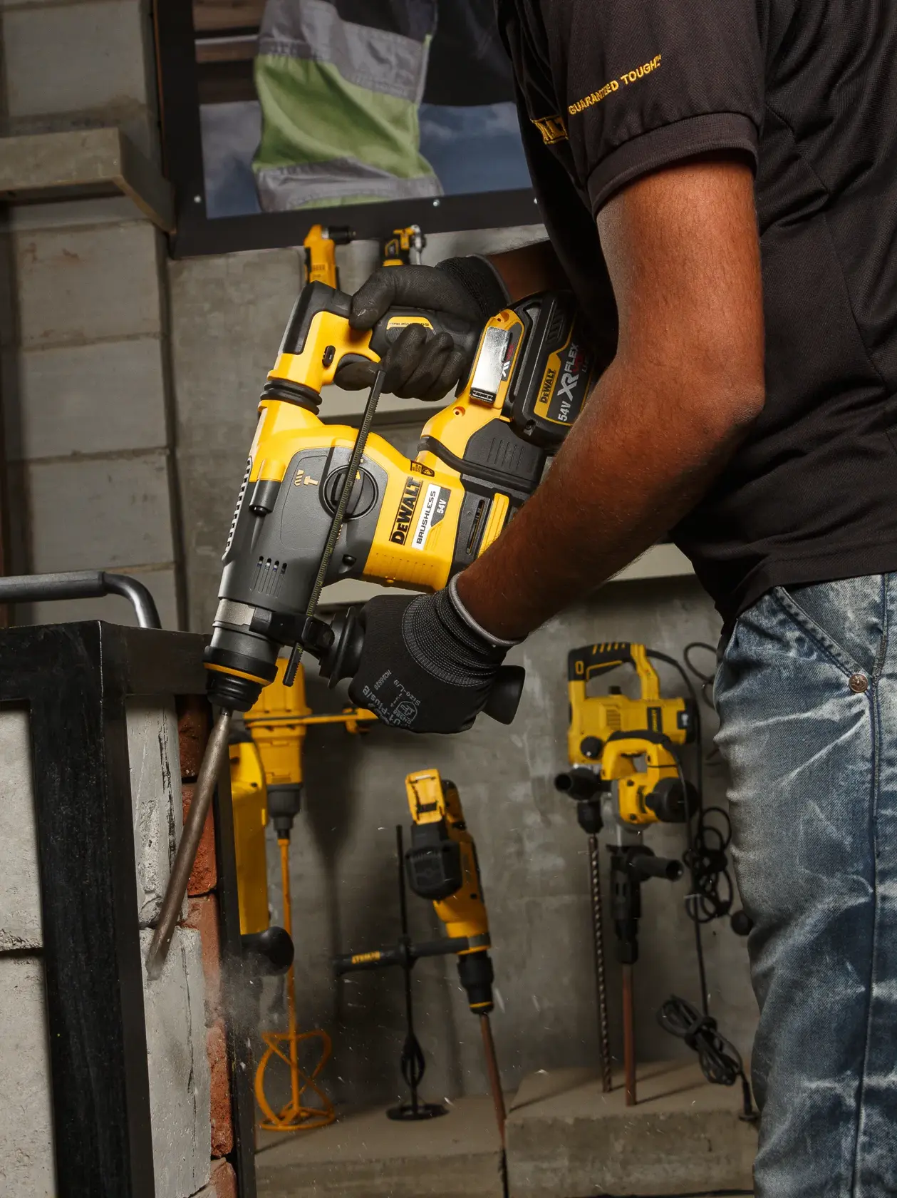 Persona usando martillo perforador DEWALT DCH333NT en pared de ladrillo. Otros equipos DEWALT al fondo.