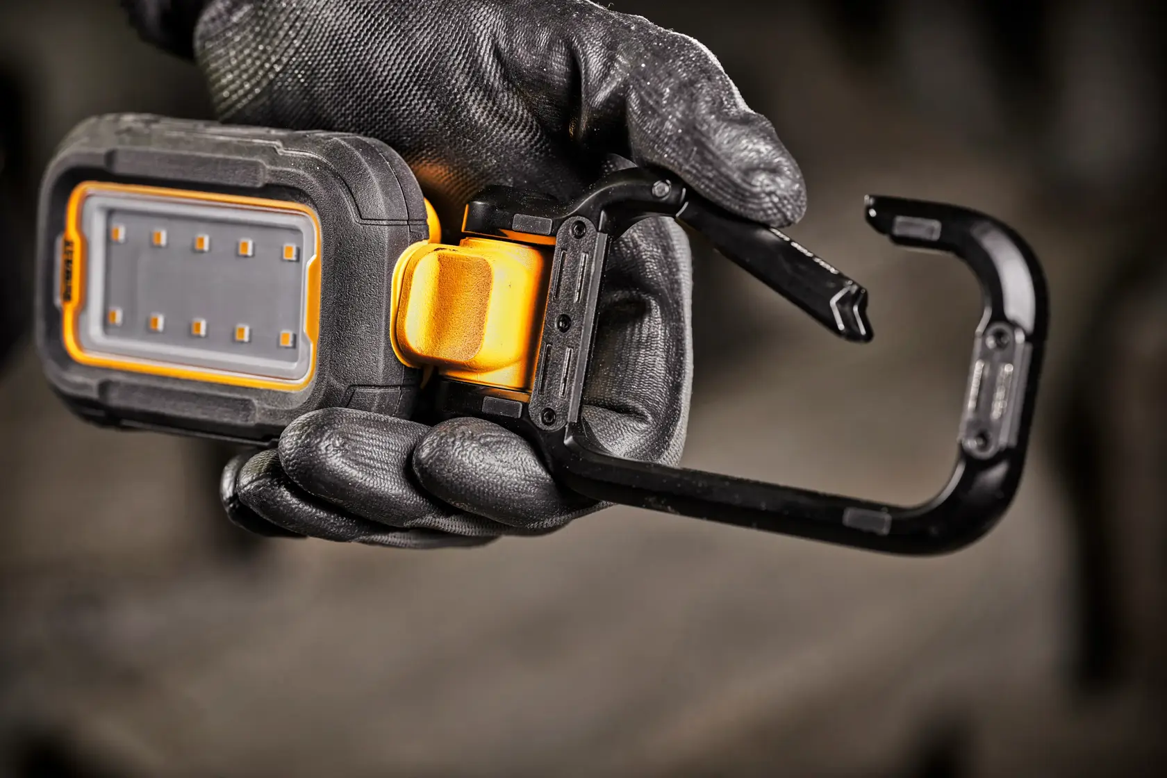 A close-up of a hand wearing a black work glove holding a DEWALT portable LED work light with an integrated black and yellow