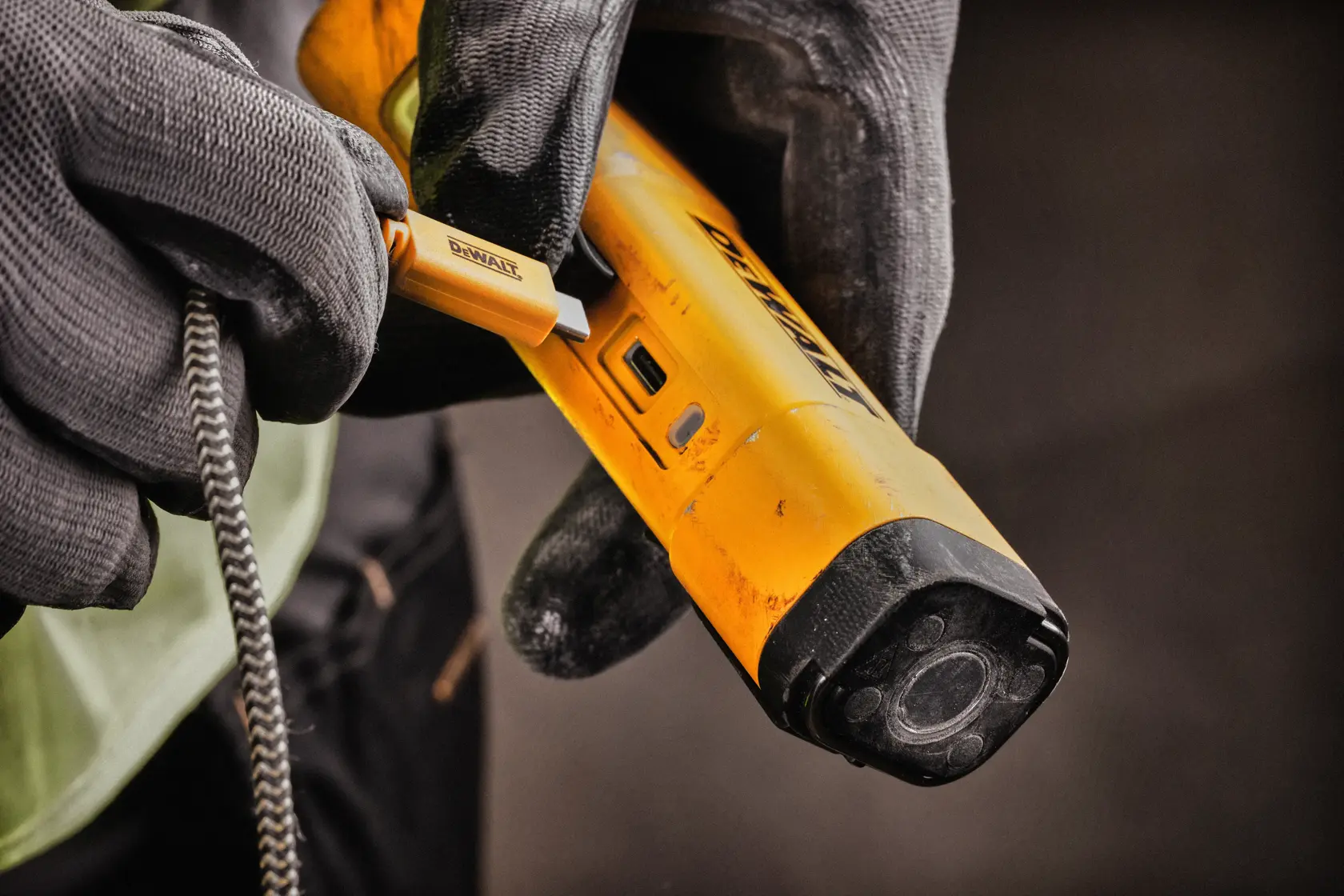 A close-up of gloved hands connecting a charging cable to a yellow DEWALT portable inspection light.