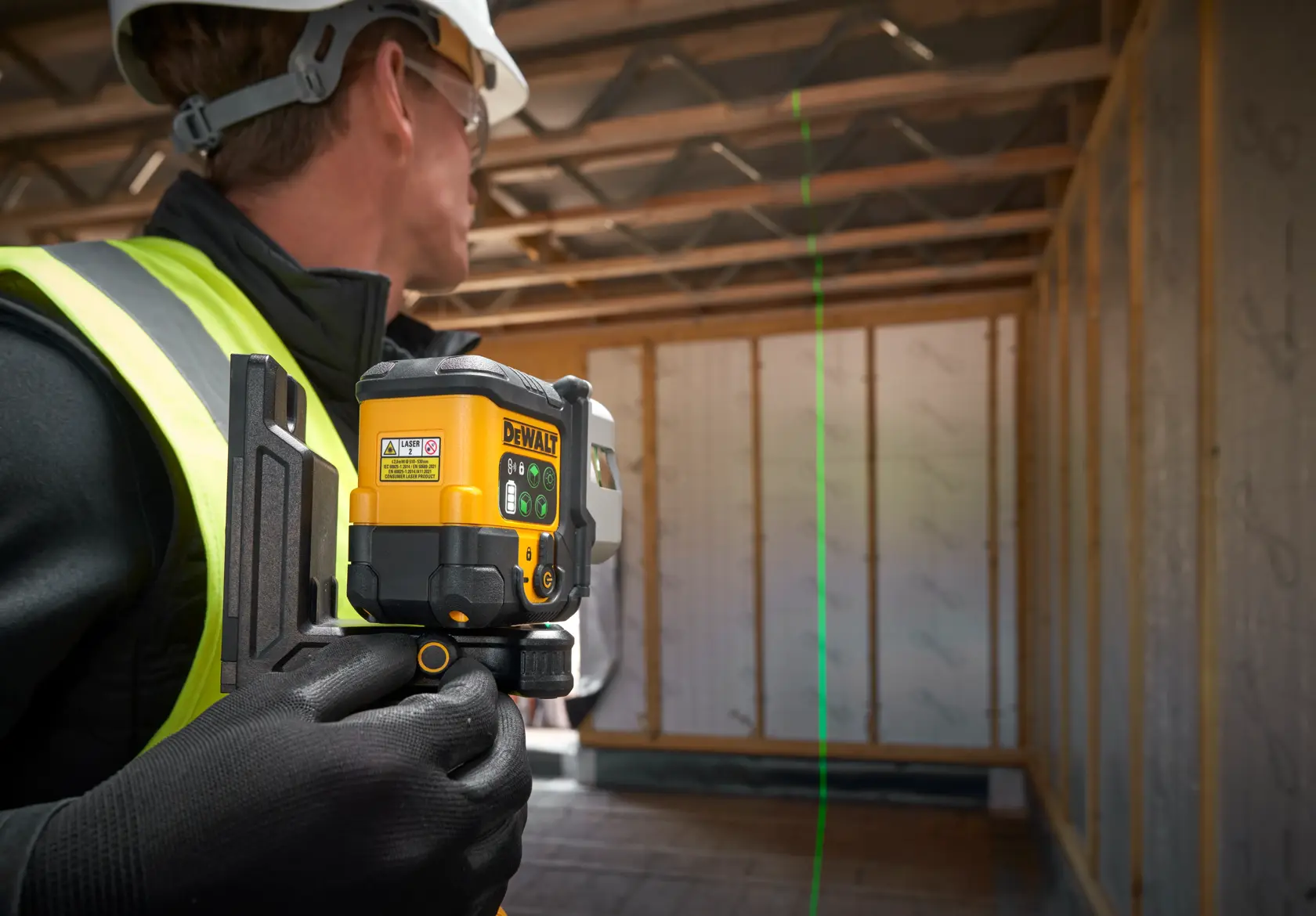 Worker uses a DEWALT green laser level for alignment in a building under construction.
