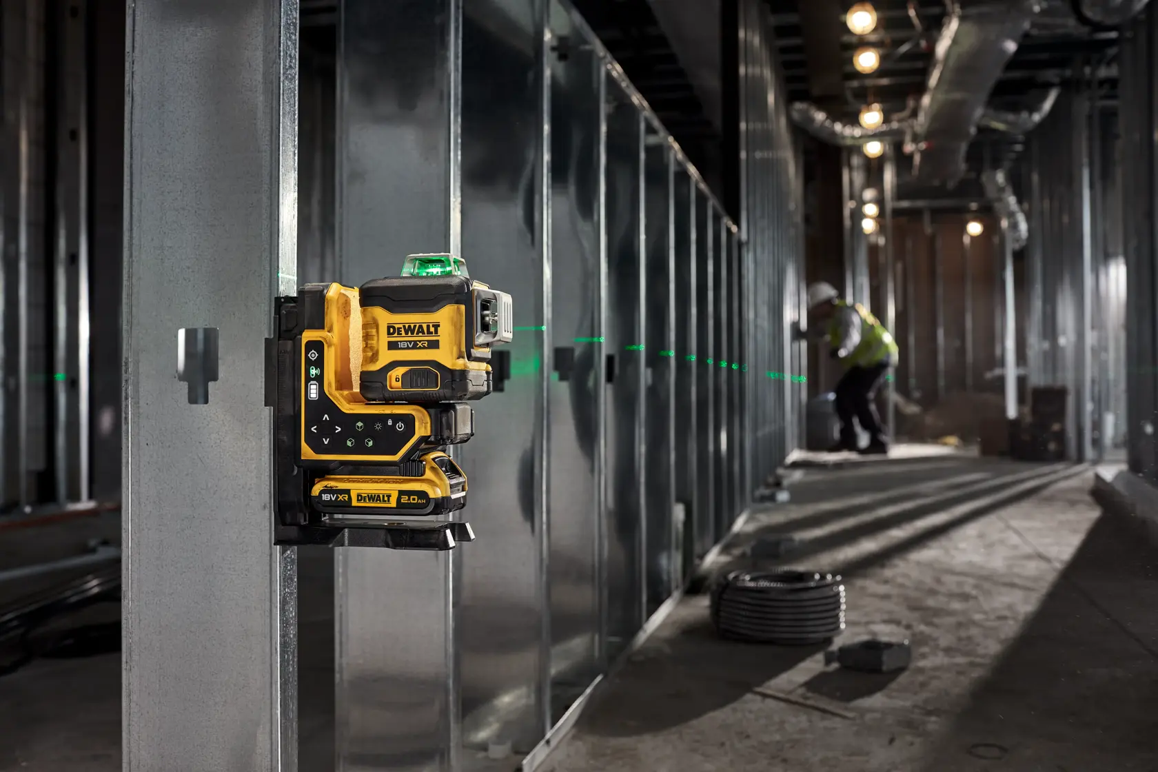 DEWALT-Laser-Nivelliergerät am Metallrahmen, grüne Linien; Arbeiter im Hintergrund auf Baustelle.