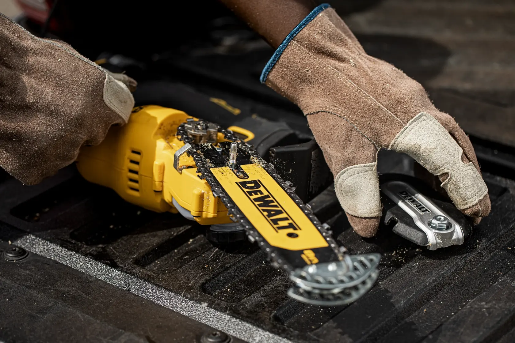 Trabajador con guantes inspecciona o monta una motosierra amarilla DEWALT sobre superficie negra.