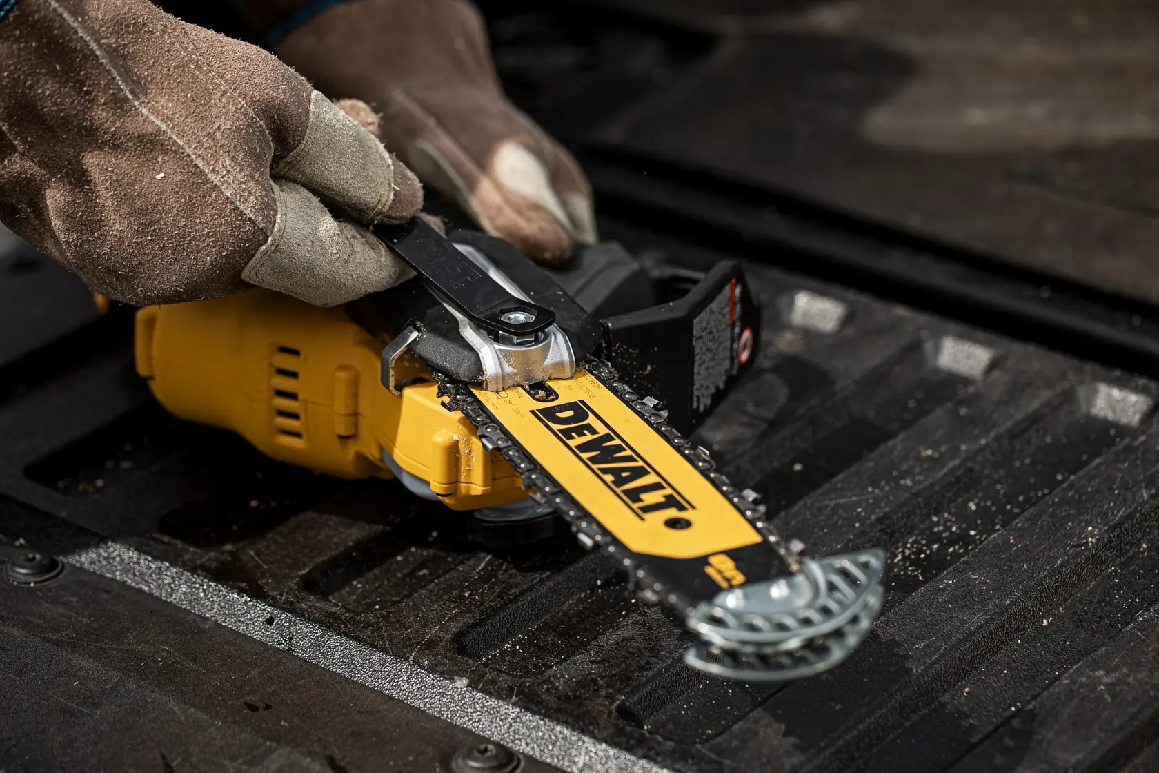 Manos con guantes ajustan la cadena de una sierra DEWALT DCMPS520N amarilla en superficie negra.