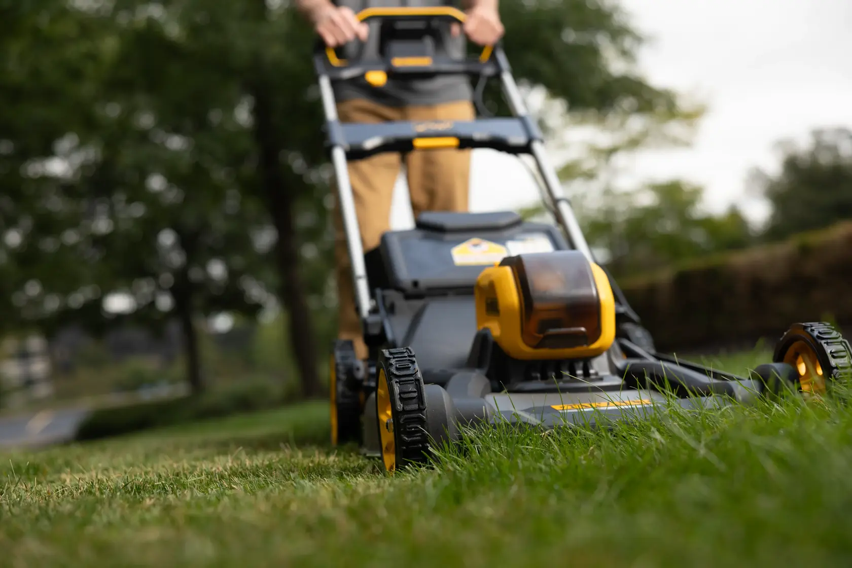 Nahaufnahme eines DEWALT Akku-Rasenmähers beim Mähen im Freien.