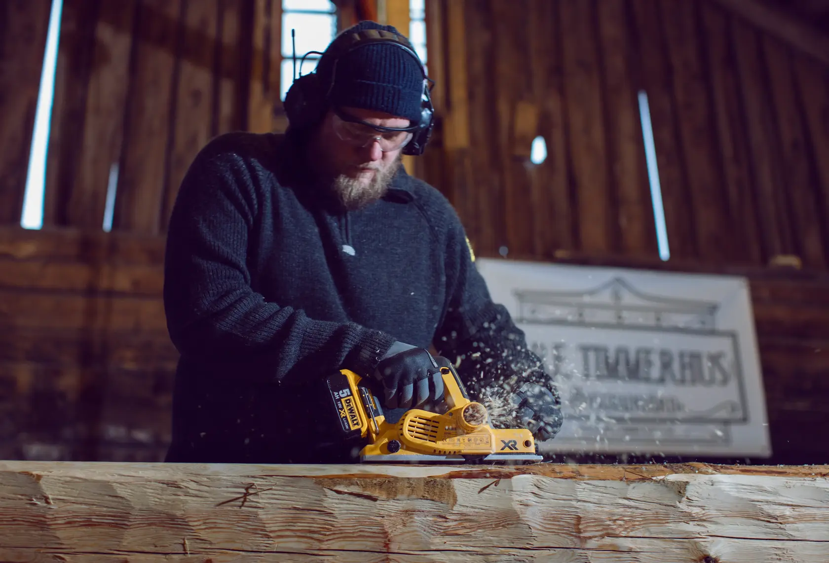 Person using a DEWALT DCP580P2 electric planer on a wooden beam in a workshop.