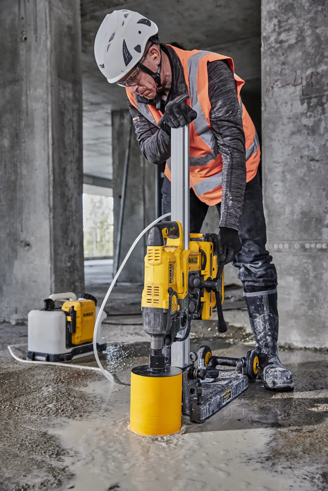A DEWALT power tool with an integrated vacuum base is being set up by a worker wearing gloves and a safety helmet on a concrete surface. The tool features yellow wheels and is connected to a hose. Text on the image reads 'Integrated vacuum base for a quick secure set-up.'