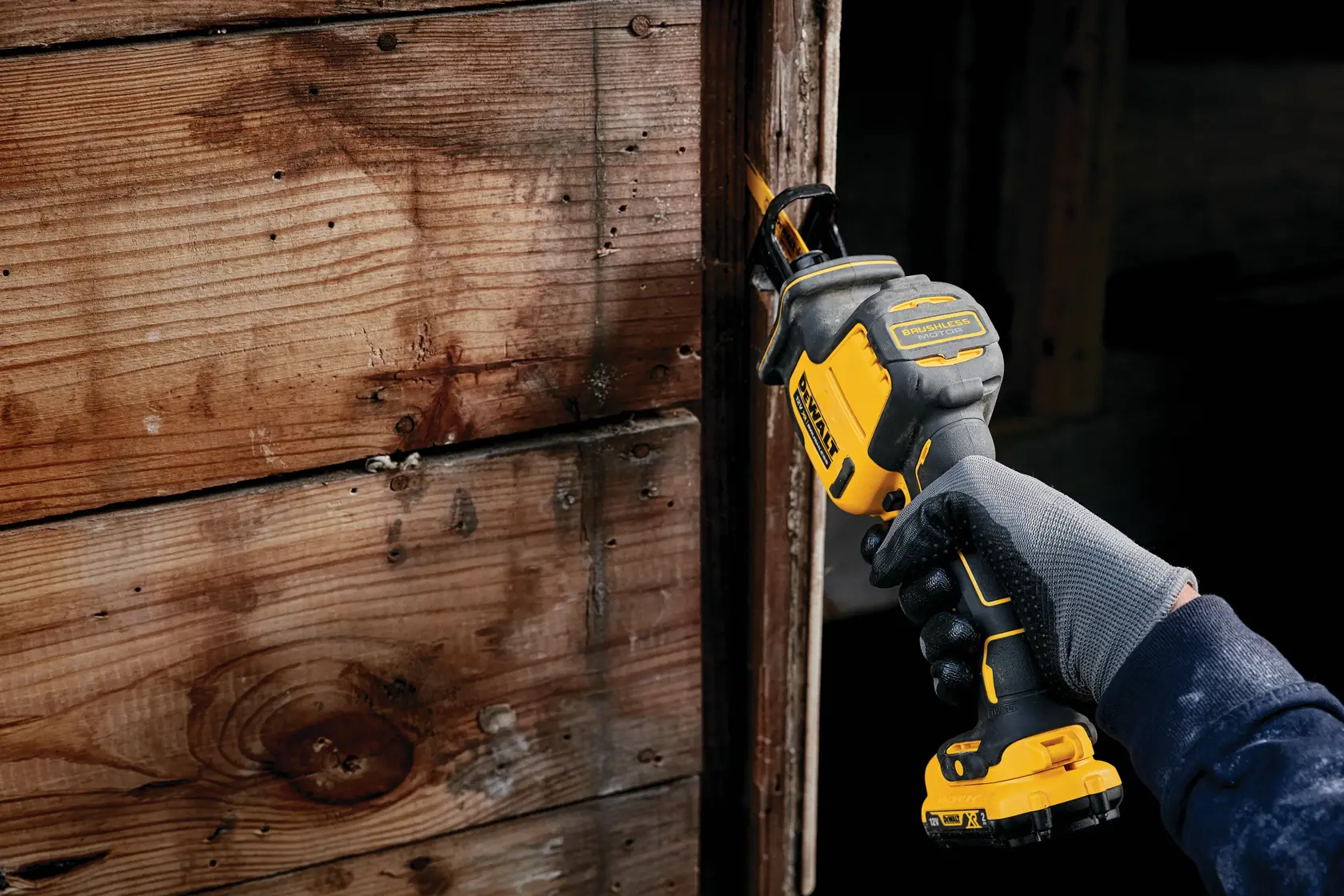 Mano enguantada usando una sierra recíproca inalámbrica DEWALT sobre madera en interior.