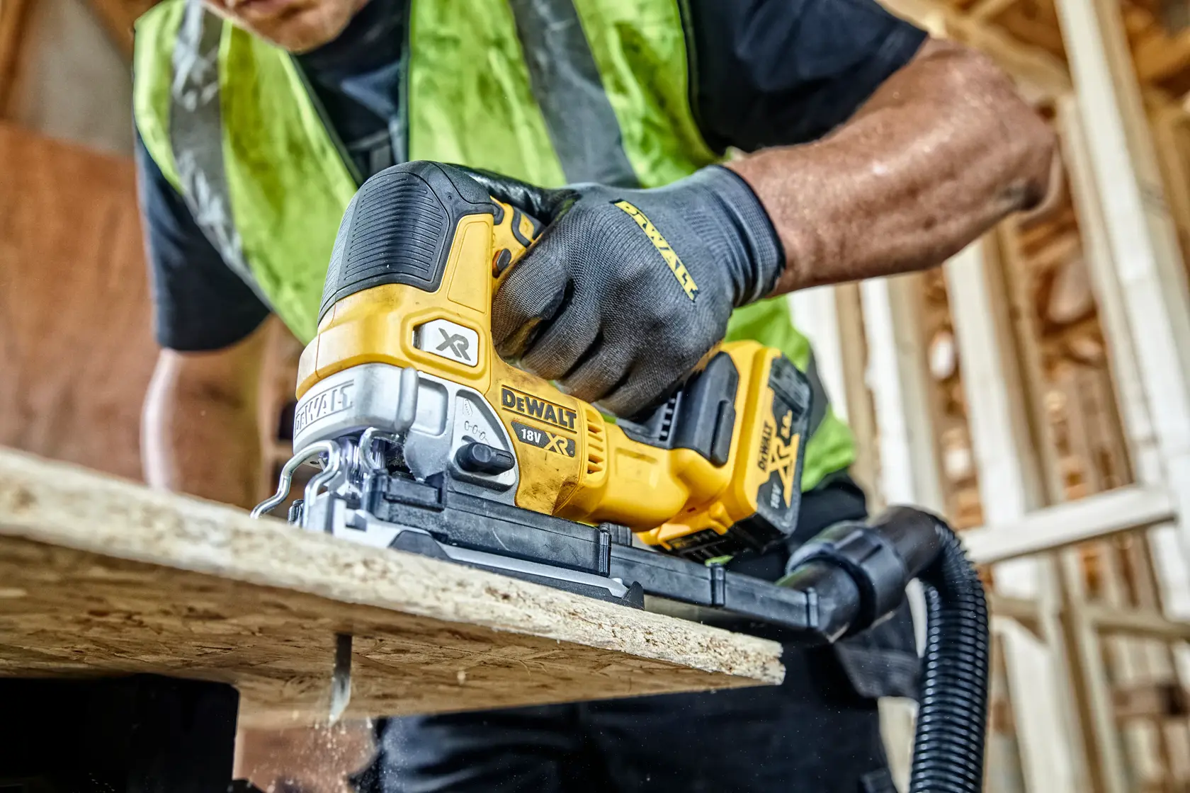 DEWALT DCS334N jigsaw cutting wood in a construction setting. Worker uses tool wearing gloves and safety vest.