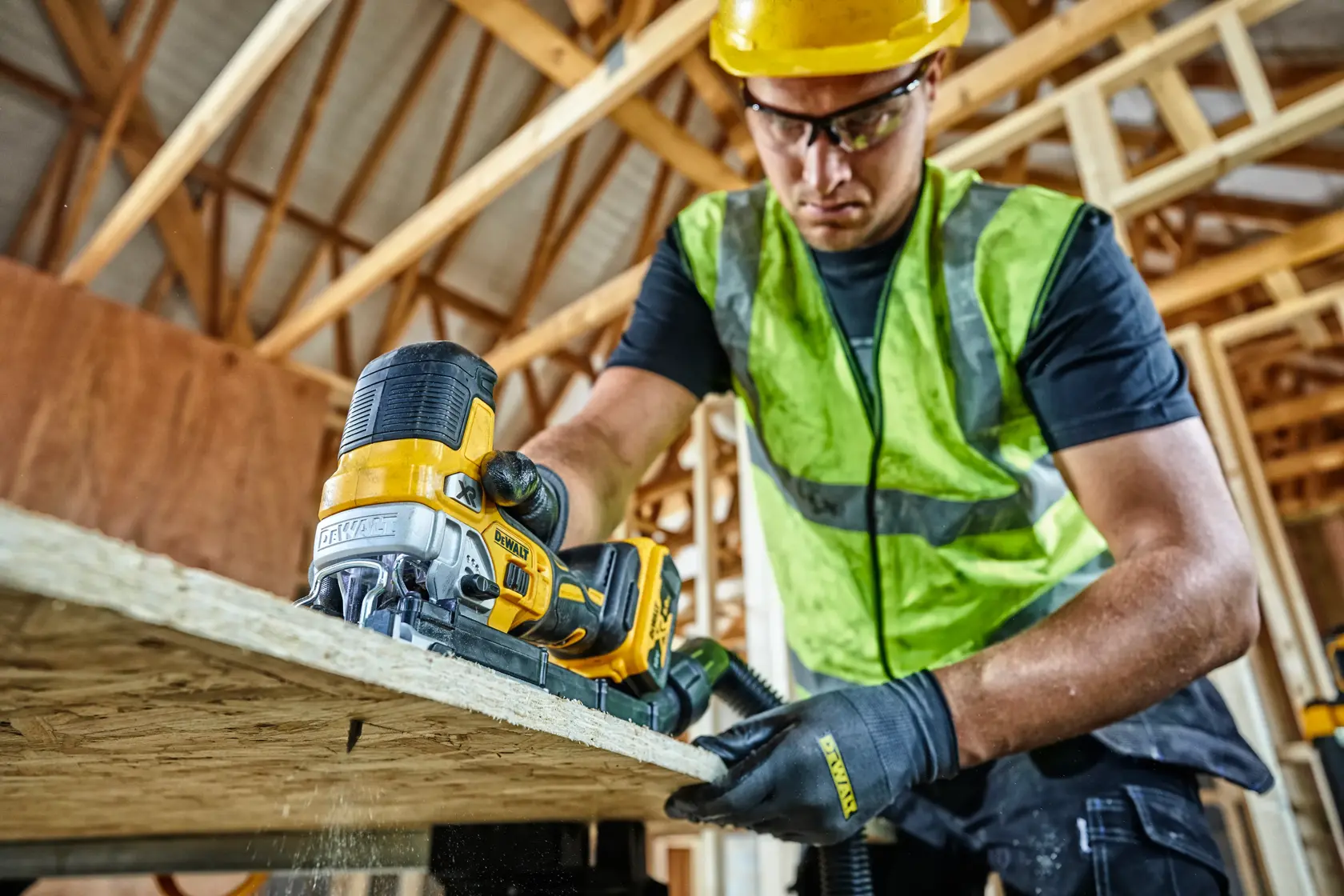 Worker uses DEWALT DCS335N jigsaw to cut wood in a construction site, wearing safety gear and gloves.