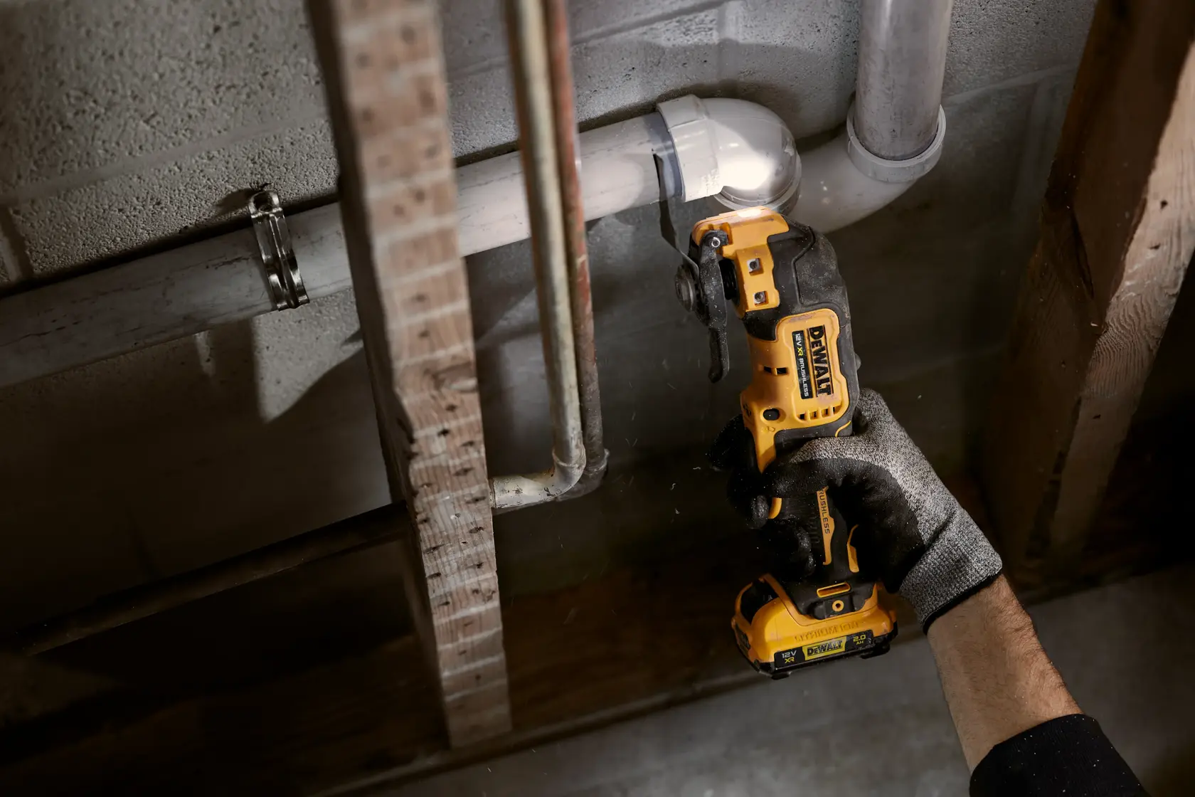 Ein DEWALT Akkuwerkzeug schneidet ein Rohr in einer Baustelle, gehalten von einer behandschuhten Hand.