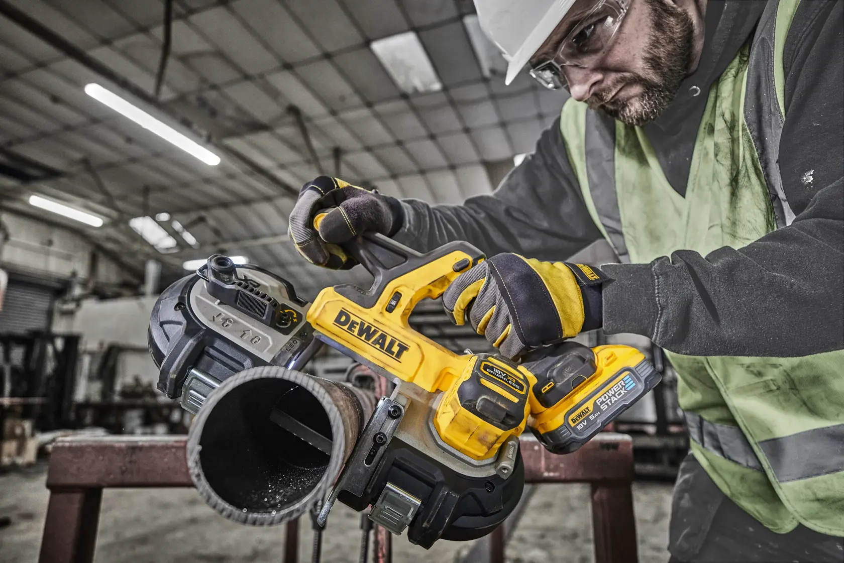 Sierra de banda inalámbrica DEWALT corta tubo metálico en taller industrial con operador con guantes.