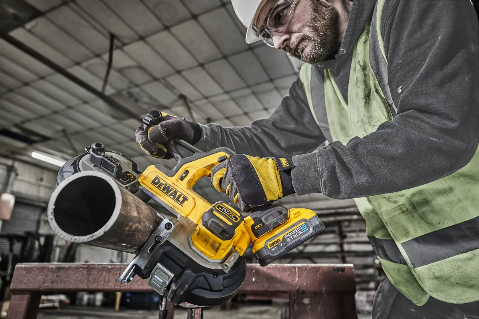 Trabajador corta tubo metálico con sierra de banda DEWALT DCS378N inalámbrica en entorno industrial.
