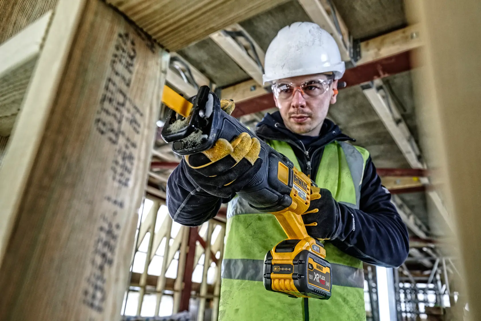 Persona usa una sierra recíproca Dewalt inalámbrica en madera, en obra, con guantes y equipo de seguridad.