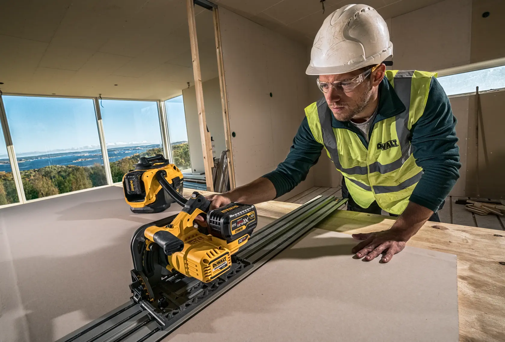 Arbeiter nutzt DEWALT Akku-Tauchsäge DCS520NT auf Holzplatte, moderne Baustelle, Sicherheitsausrüstung.
