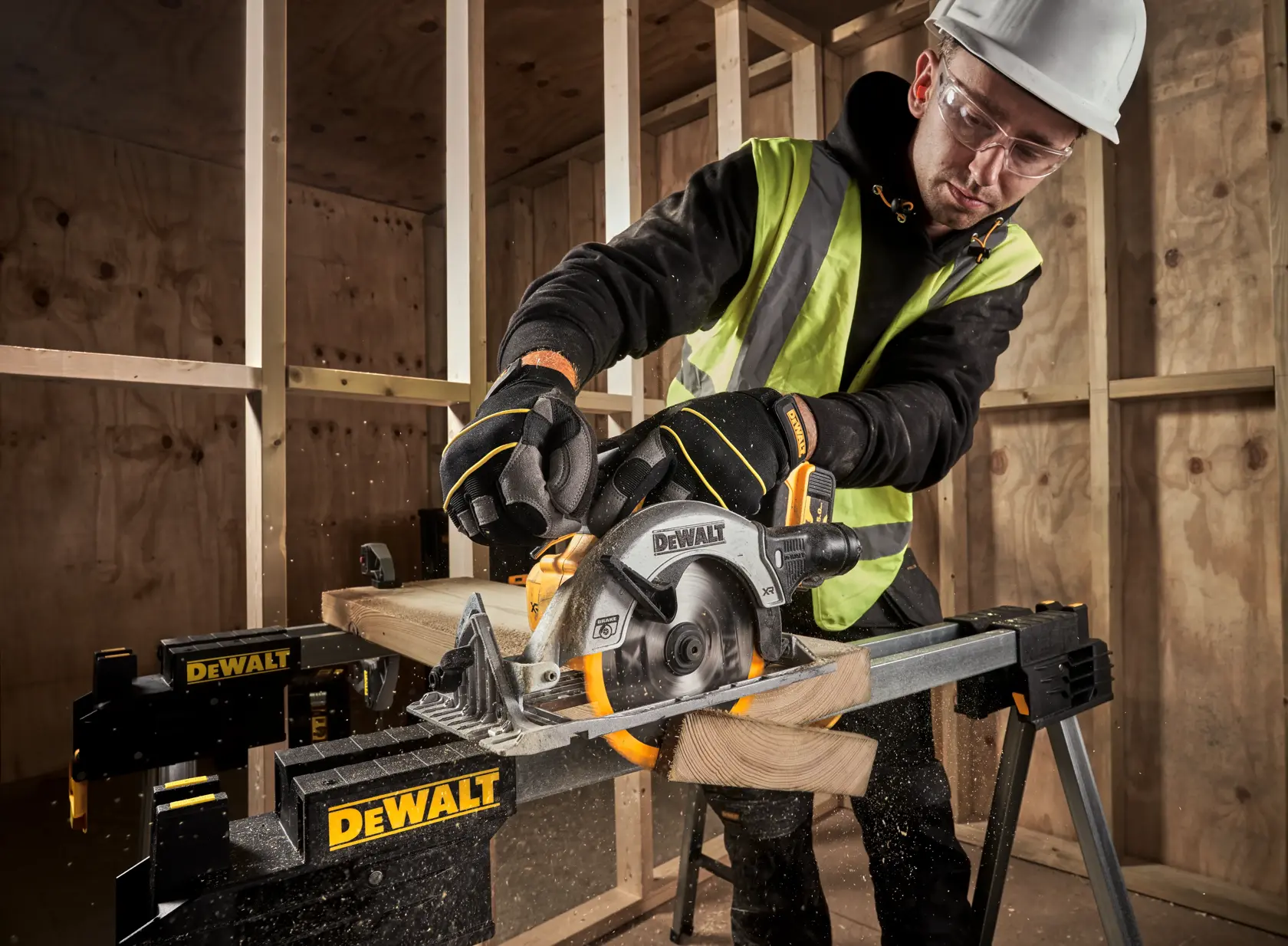 Person using DEWALT DCS565N circular saw to cut wood on a DEWALT workbench at a construction site.