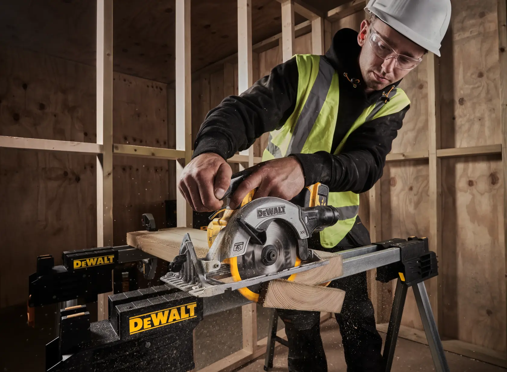 DEWALT DCS565N circular saw cutting wood, operator in a hi-vis vest and hard hat, indoors on a construction site.