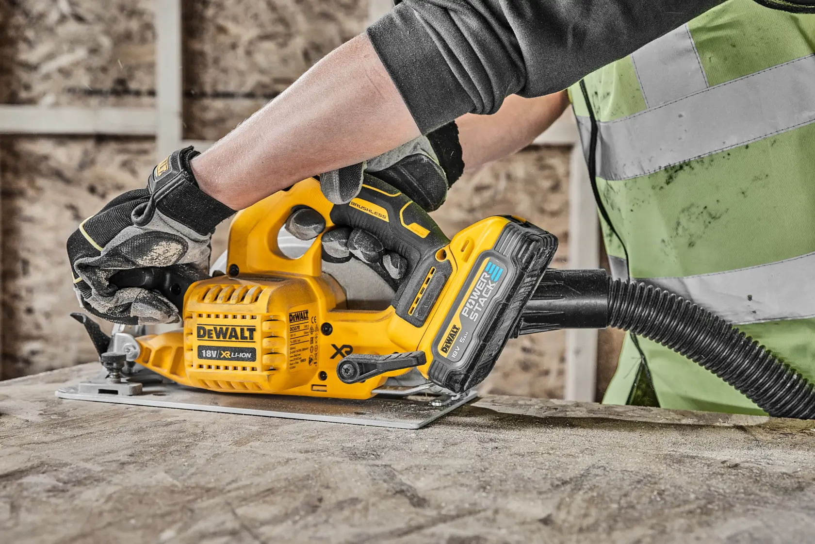 Person uses a DEWALT cordless circular saw with dust extraction on a wooden surface at a construction site.