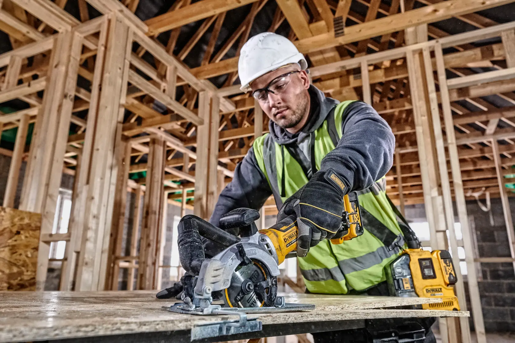 Worker uses a DEWALT DCS571N cordless saw to cut wood on a construction site with timber framing.